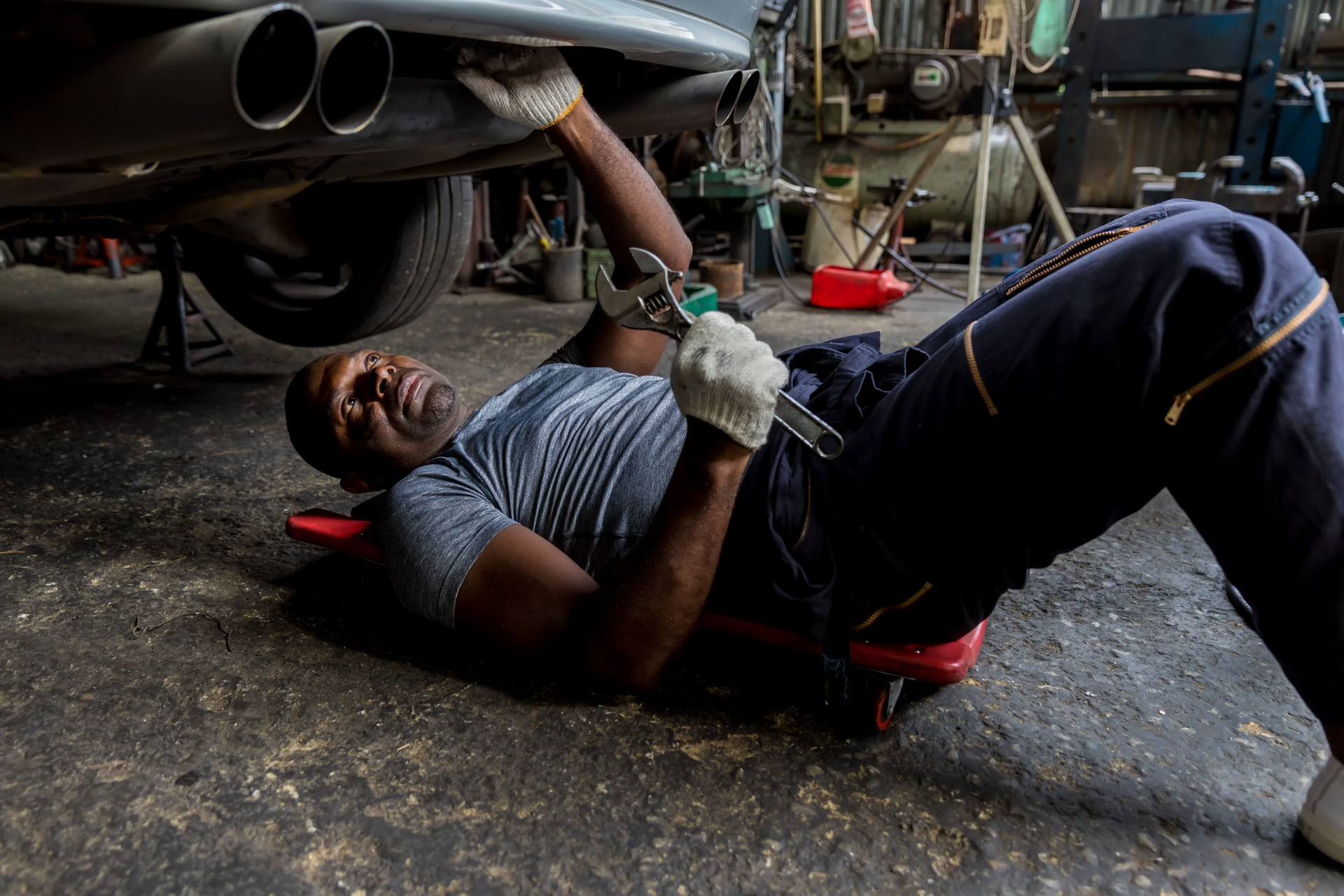 Mechanic lying down and working under car at auto service garage. Technician vehicle maintenance and checking under car at automotive motor garage.