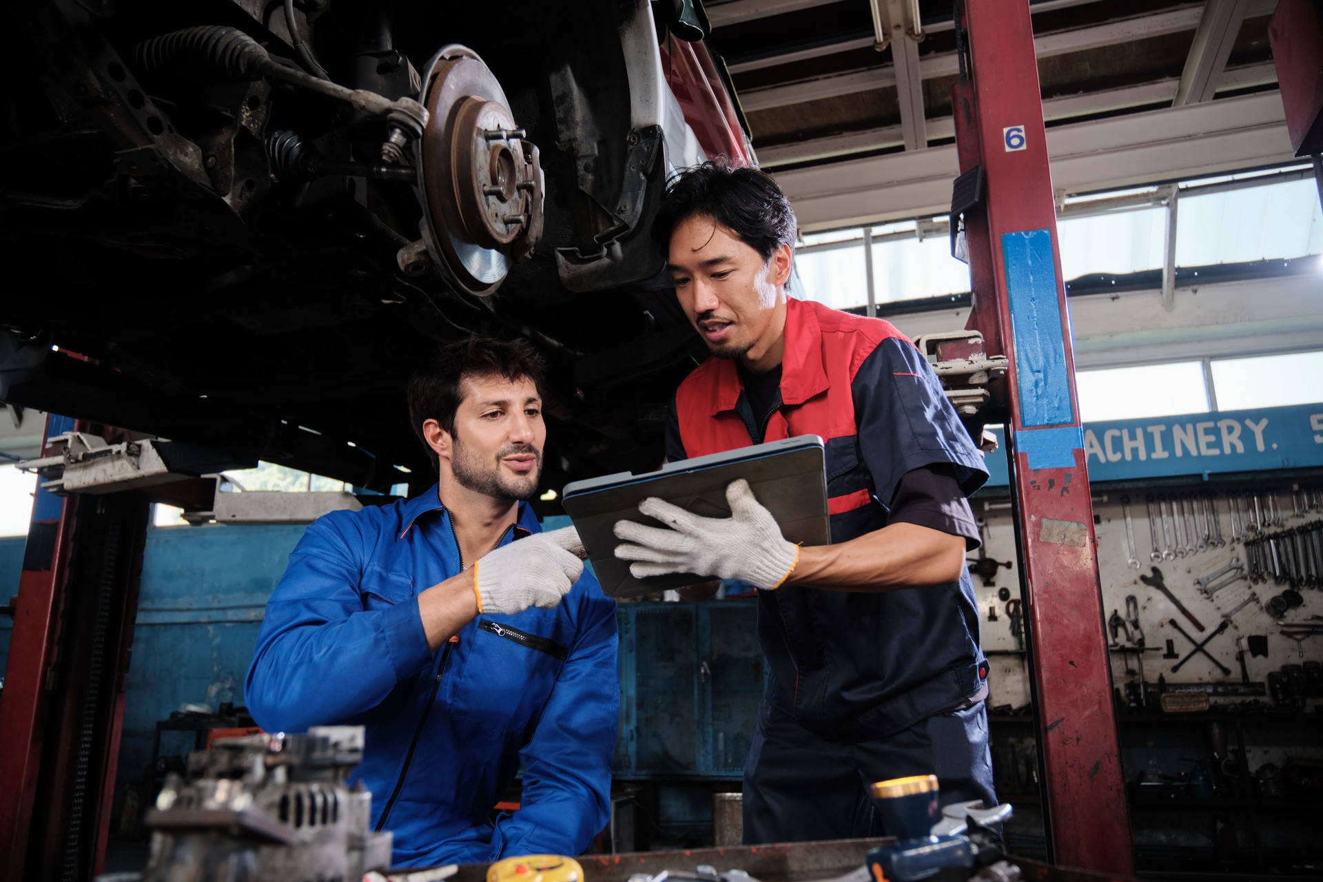 Two male mechanics fixing automotive wheels and car suspensions in garage.